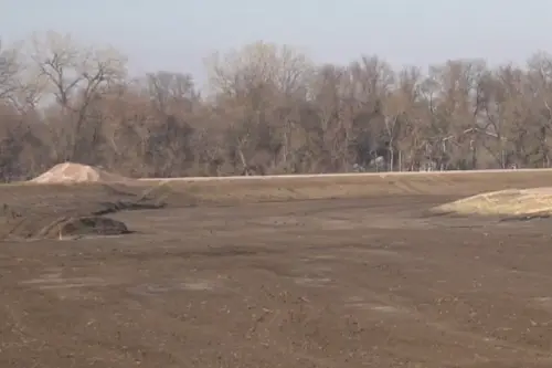 A dirt field with a dirt pile in the middle, surrounded by open space and under a hazy sky.